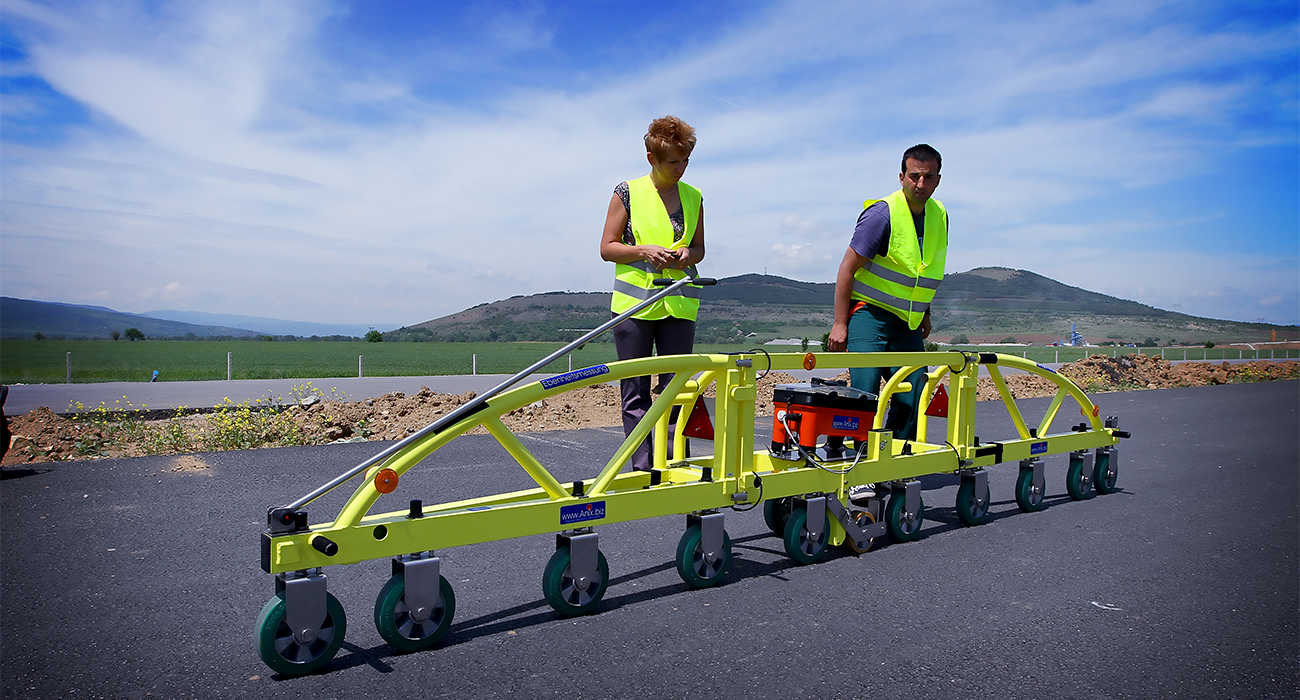 Road Company employees with reflective vests testing a pavement testing device on a paved road.