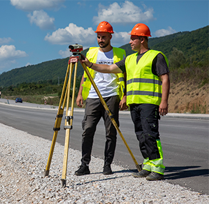 Employees from Patstroy 92 on a job site wearing safety helmets surveying with surveying equipment.