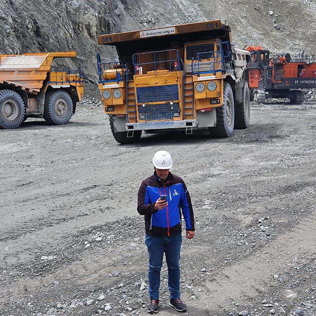 An employee of Ellatzite-Med in work clothes and safety helmet in front of construction machinery on a job site.