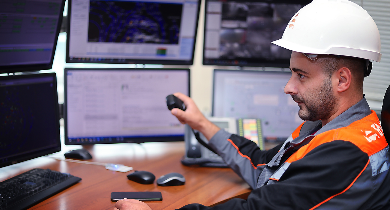 Employee of Ellatzite Med wearing work clothes and safety helmet looking at information from monitors.
