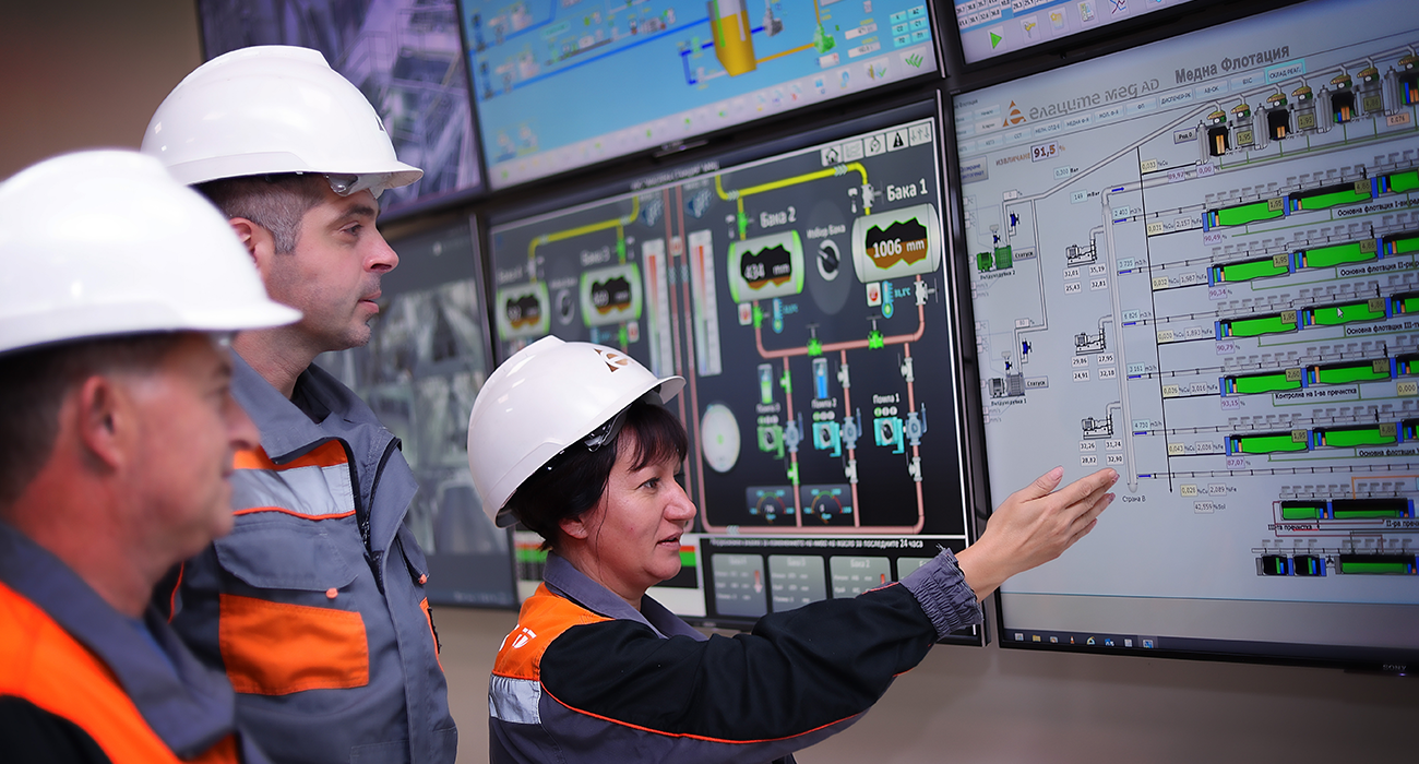 Employees from Ellazite Med wearing work clothes and safety helmets discussing information from work software.