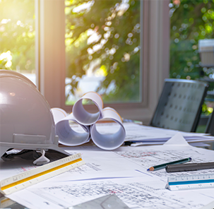 Desk with building plans, telephone, tape measure and safety helmet.