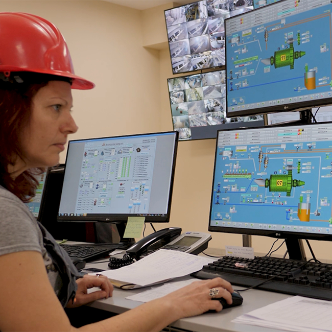 A woman in a safety helmet focused on multiple computer screens, working with an industrial design program.