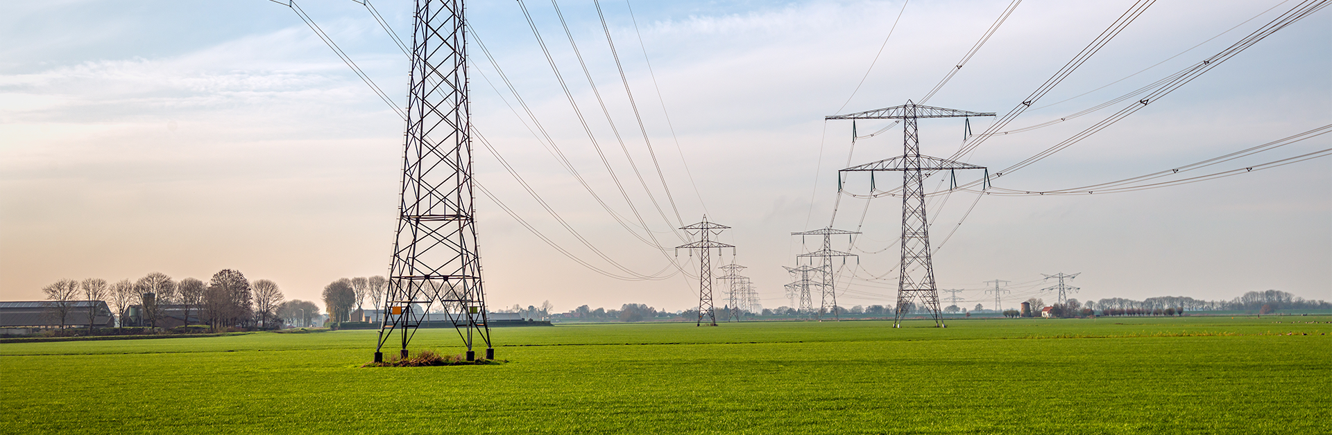 High voltage power lines with metal poles located in a green field.