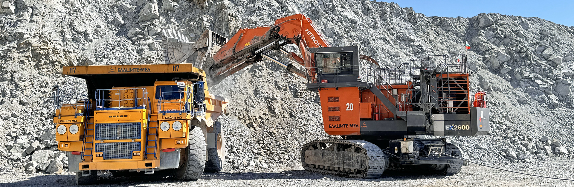 Excavator and dump truck at a work site next to a sand embankment.